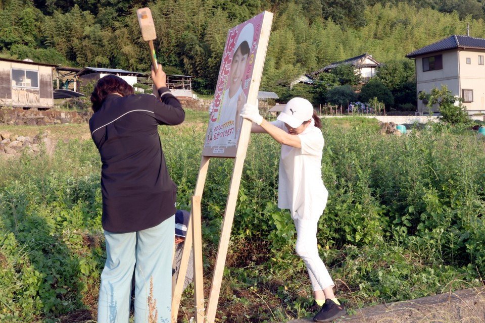 事務所のスタッフと共に看板立てをするはた総支部長(右) はたともこ
